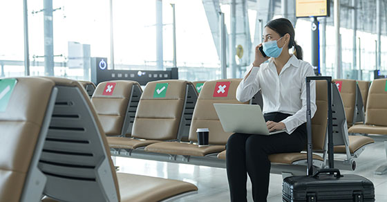 Social distancing businesswoman wearing face mask sit working with laptop keeping distance away from each other to avoid covid19 infection during pandemic Empty chair seat red cross shows new normal Demo