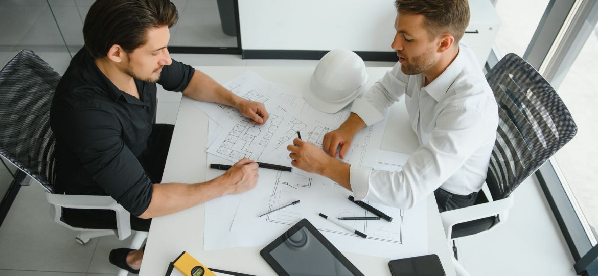 two people sit in front of construction plan and talk about the architecture