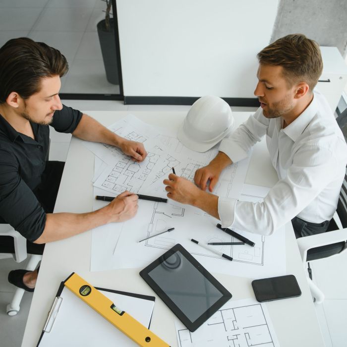 two people sit in front of construction plan and talk about the architecture